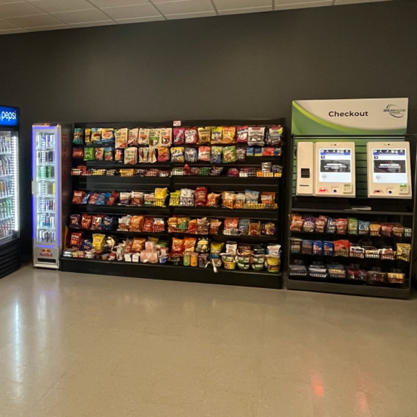 Micro-market wall of refrigerated cases and snack shelving in a workplace break room